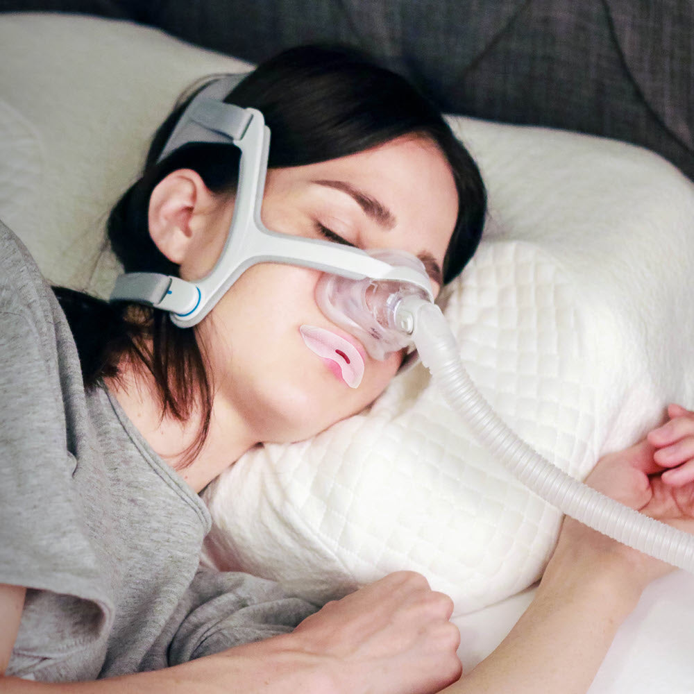 Woman lying in bed using a CPAP machine with mouth tape